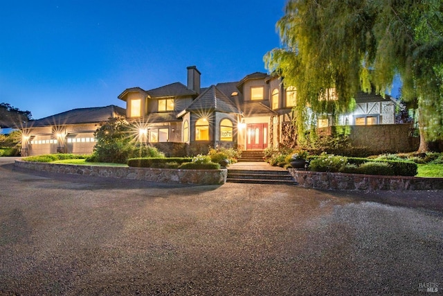view of front facade featuring stucco siding, a chimney, driveway, and an attached garage