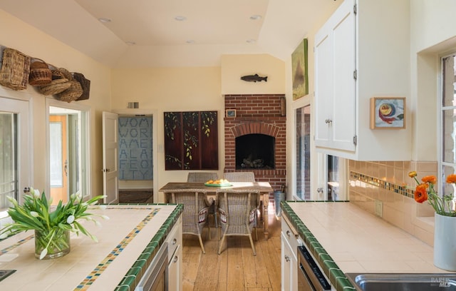 2480 Spring Mountain Rd, Saint Helena, CA 94574 - kitchen with tile countertops, white cabinets, light wood-style floors, a brick fireplace, and dishwashing machine