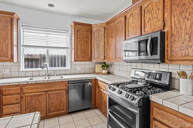 kitchen featuring light tile patterned floors, brown cabinets, tasteful backsplash, a sink, and appliances with stainless steel finishes