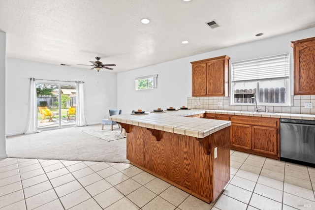 kitchen with a sink, visible vents, tile countertops, dishwasher, and light colored carpet