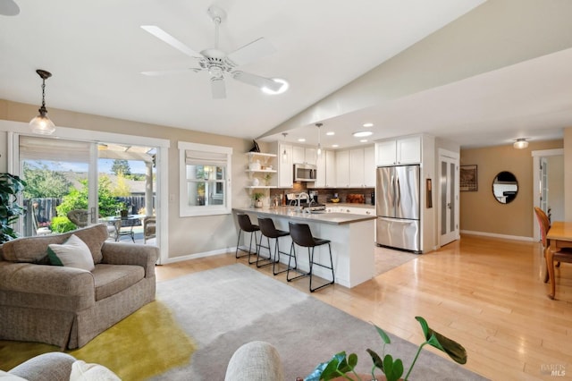 living area with vaulted ceiling, baseboards, a ceiling fan, and light wood-type flooring