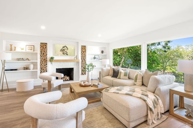 living area with wood finished floors, built in shelves, a fireplace, and plenty of natural light