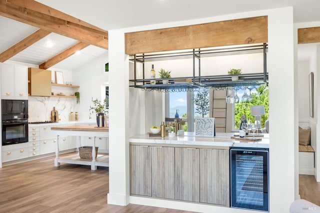bar featuring vaulted ceiling with beams, tasteful backsplash, black appliances, wood finished floors, and beverage cooler