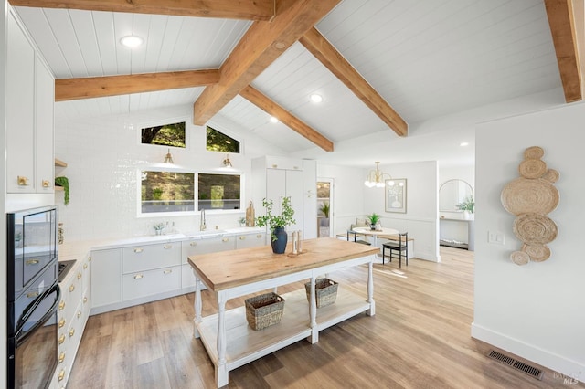 kitchen with light wood-style floors, vaulted ceiling with beams, visible vents, white cabinetry, and light countertops