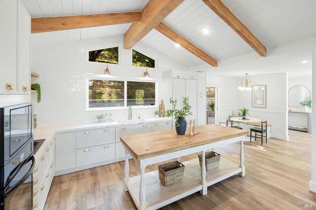 kitchen featuring a sink, light wood-style floors, light countertops, oven, and vaulted ceiling with beams