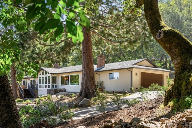 ranch-style house featuring a sunroom, a garage, a shingled roof, stairs, and a chimney