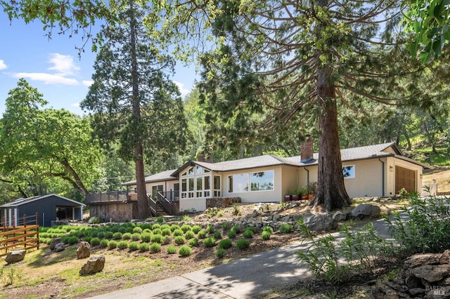 view of front of house featuring a chimney, an attached garage, stucco siding, stairway, and a sunroom