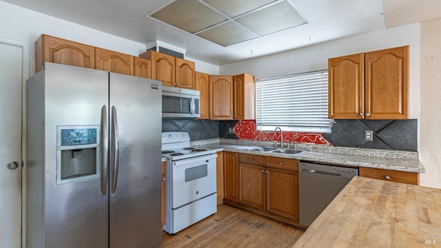 kitchen featuring a sink, decorative backsplash, brown cabinetry, appliances with stainless steel finishes, and wood finished floors