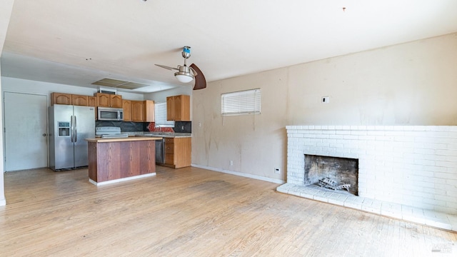kitchen featuring light wood-style flooring, appliances with stainless steel finishes, light countertops, a center island, and open floor plan