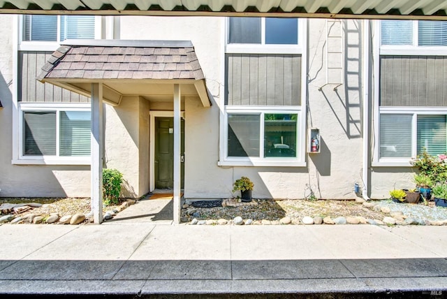 entrance to property featuring roof with shingles and stucco siding
