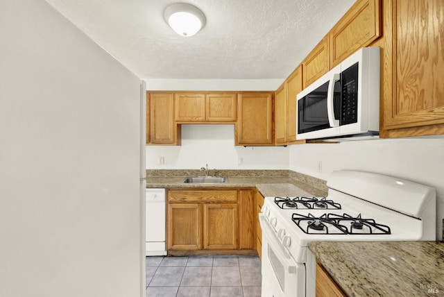 kitchen with white appliances, light stone countertops, a textured ceiling, a sink, and light tile patterned floors