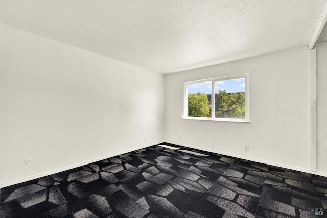 carpeted spare room featuring a textured ceiling and baseboards
