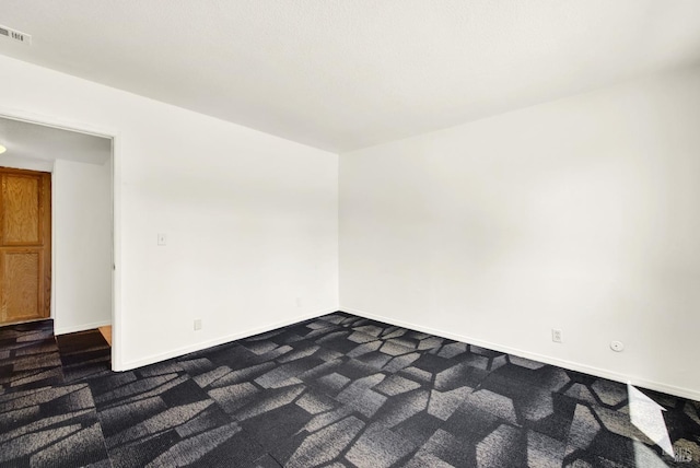 empty room featuring dark carpet, baseboards, and visible vents