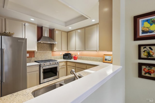 kitchen featuring wall chimney range hood, stainless steel appliances, recessed lighting, and a tray ceiling