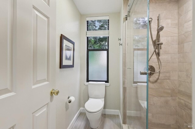 full bath featuring baseboards, tiled shower, toilet, and wood finished floors