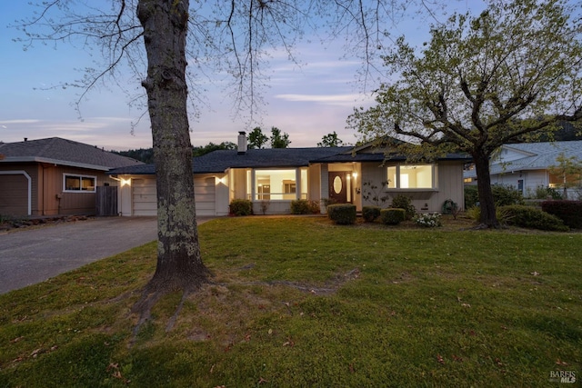 ranch-style house featuring concrete driveway, a lawn, an attached garage, and a chimney