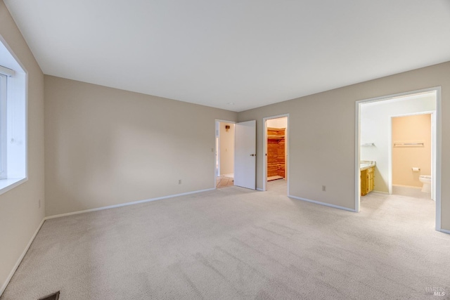 unfurnished bedroom featuring baseboards, a walk in closet, light carpet, and ensuite bathroom