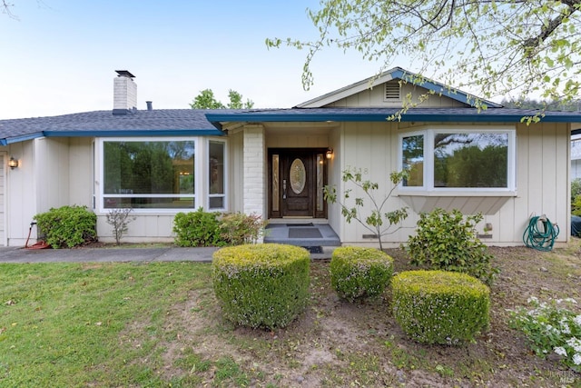 view of front of home featuring a chimney, a shingled roof, and a front yard