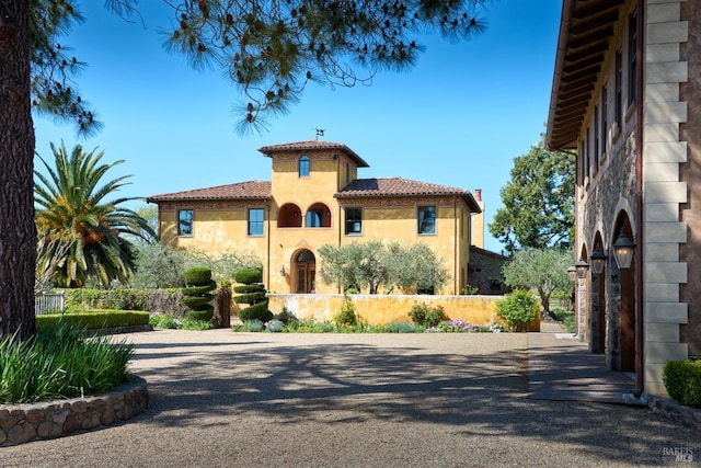 mediterranean / spanish-style home with fence, stucco siding, and a tile roof