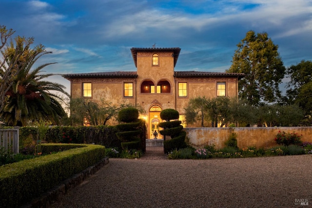 mediterranean / spanish home with gravel driveway, fence, and stucco siding