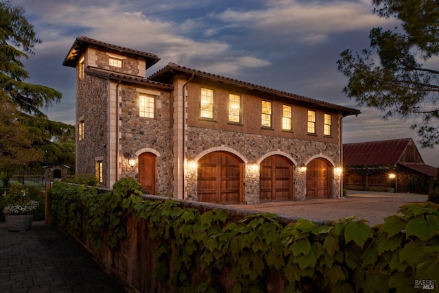 mediterranean / spanish house featuring a tiled roof, an attached garage, driveway, and stone siding