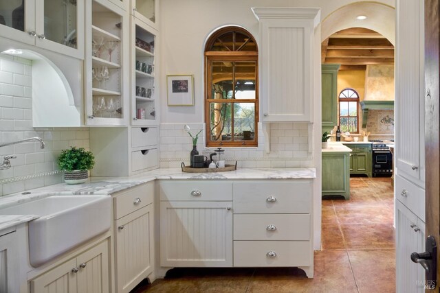 kitchen featuring light tile patterned flooring, light stone counters, a sink, tasteful backsplash, and glass insert cabinets