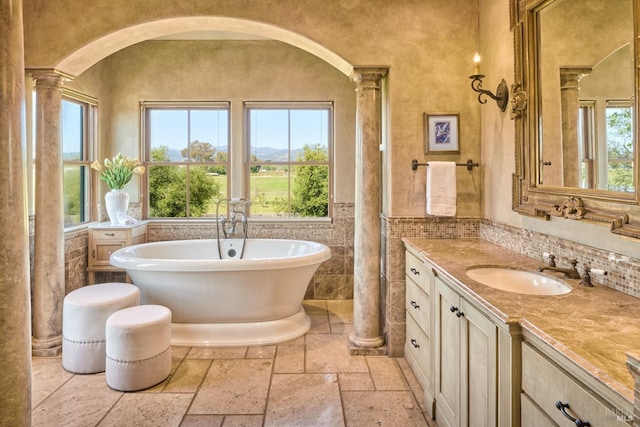 full bath with stone tile floors, ornate columns, plenty of natural light, and vanity