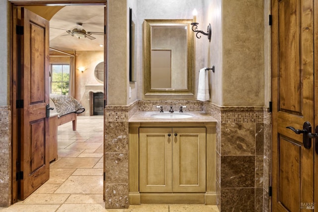 bathroom featuring vanity, stone tile floors, a glass covered fireplace, and a ceiling fan