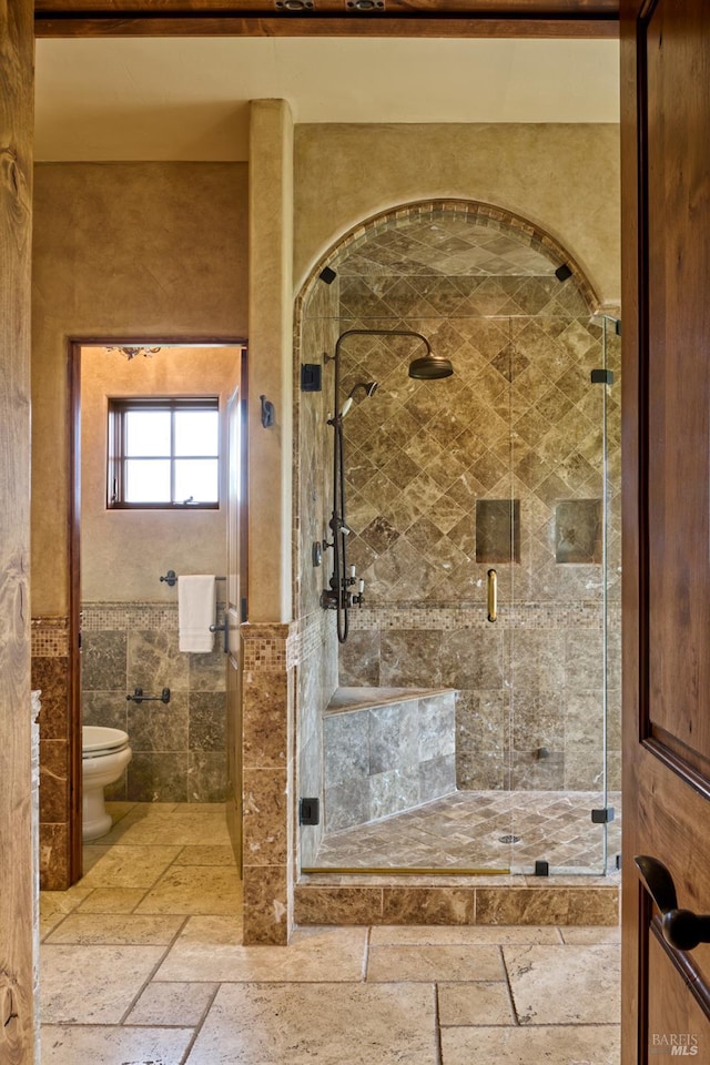 full bath featuring tile walls, a stall shower, toilet, and stone tile flooring