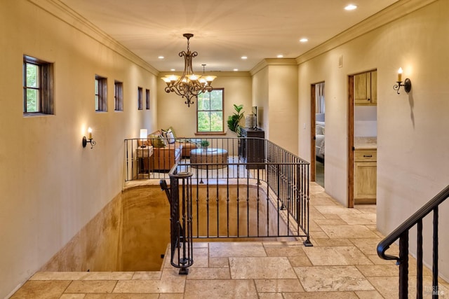 corridor featuring an inviting chandelier, ornamental molding, an upstairs landing, and stone tile flooring