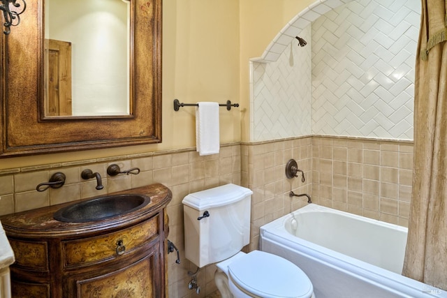 bathroom with a washtub, tile walls, wainscoting, vanity, and toilet