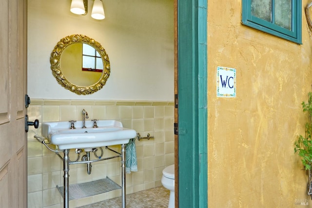 half bathroom featuring toilet, tile walls, tile patterned floors, a wainscoted wall, and a sink