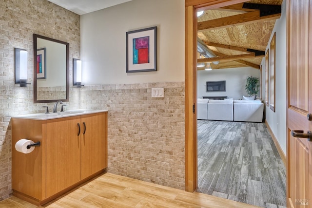 bathroom featuring brick wall, vanity, beamed ceiling, and wood finished floors
