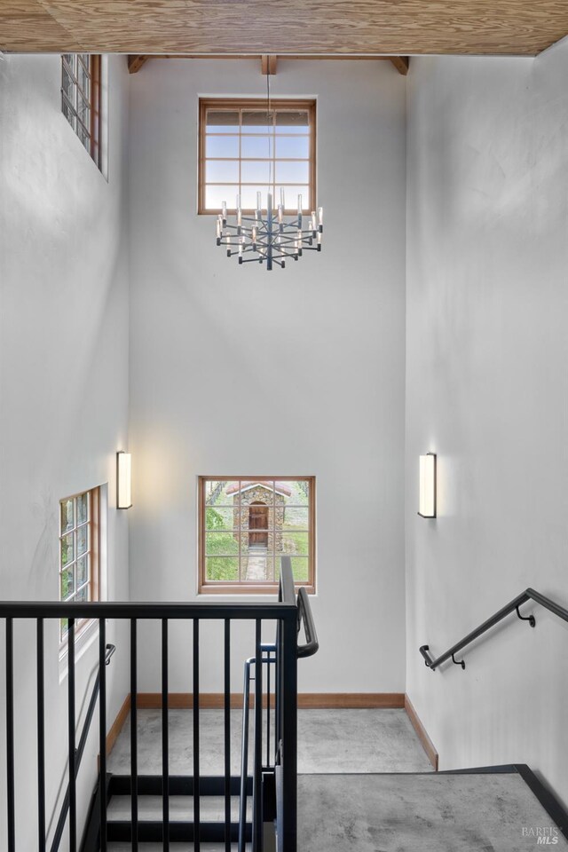 staircase featuring a high ceiling, a notable chandelier, a wealth of natural light, and baseboards