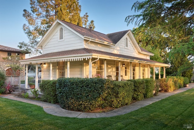view of side of property featuring a lawn, covered porch, and a shingled roof