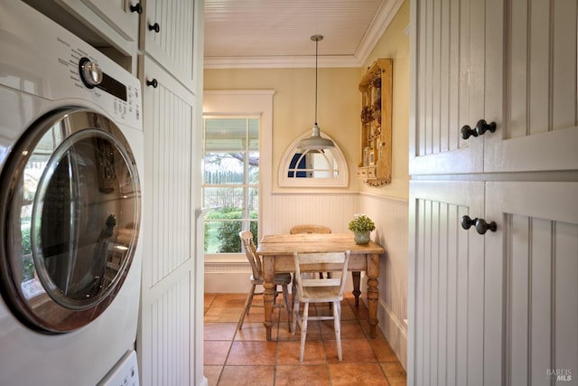 washroom with crown molding, stacked washing maching and dryer, a wainscoted wall, and cabinet space