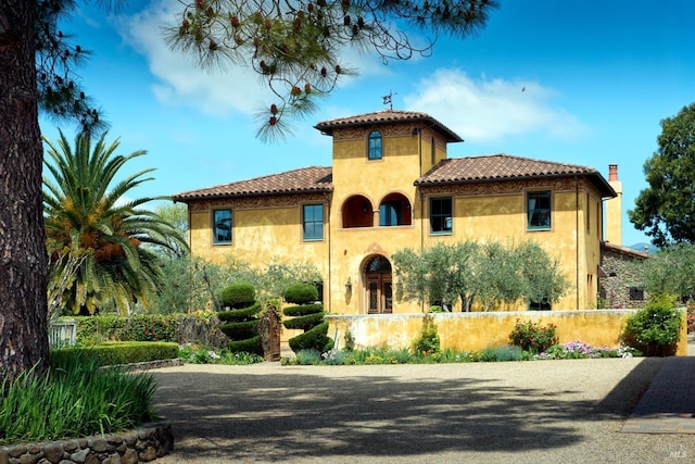 mediterranean / spanish house featuring stucco siding, a tile roof, and fence
