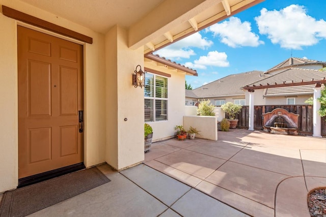 view of exterior entry featuring stucco siding, fence, and a patio