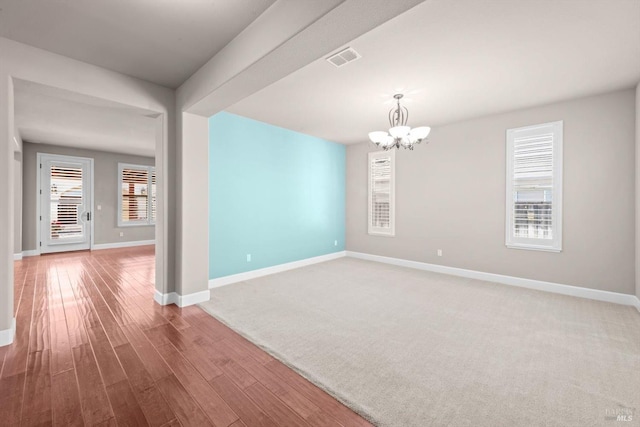 empty room featuring baseboards, a notable chandelier, a healthy amount of sunlight, and visible vents
