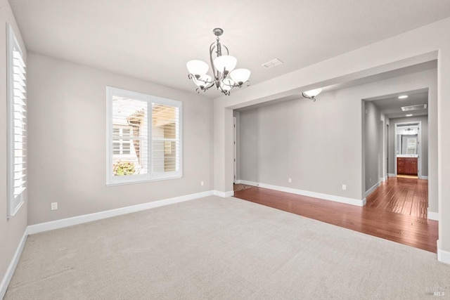 carpeted spare room with a chandelier and baseboards