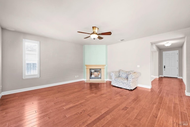unfurnished room with visible vents, ceiling fan, light wood-style flooring, baseboards, and a glass covered fireplace