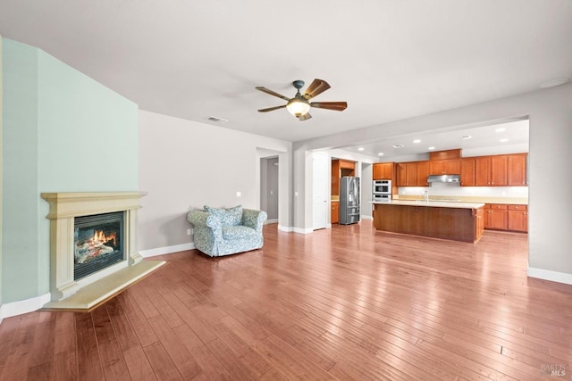 unfurnished living room with light wood-type flooring, baseboards, visible vents, and ceiling fan