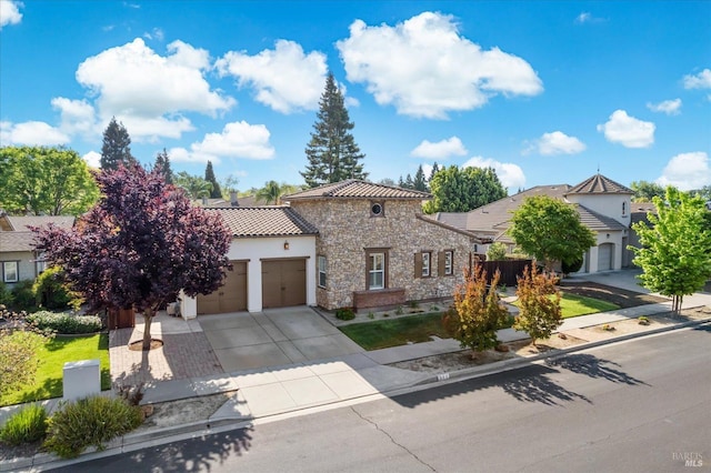 mediterranean / spanish home with stone siding, a garage, stucco siding, a tile roof, and driveway