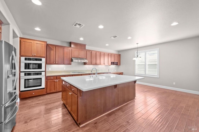 kitchen with a center island with sink, baseboards, white appliances, under cabinet range hood, and light countertops