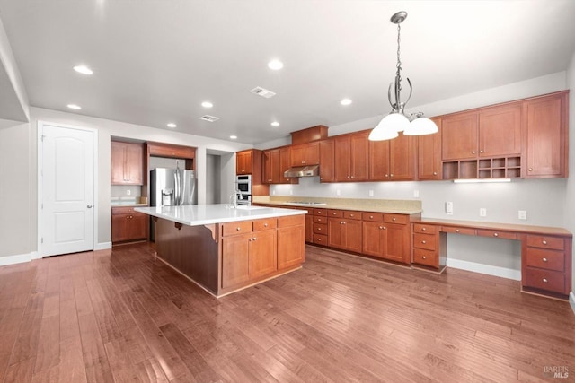 kitchen with brown cabinetry, wood-type flooring, light countertops, baseboards, and appliances with stainless steel finishes