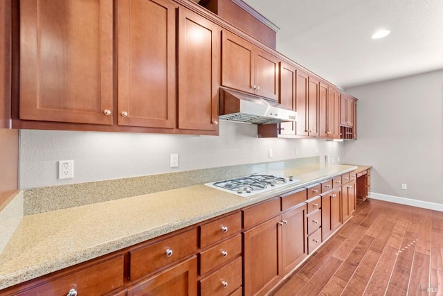 kitchen with brown cabinets, under cabinet range hood, white gas stovetop, baseboards, and light wood-style floors