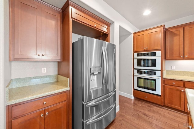 kitchen featuring brown cabinetry, light stone counters, light wood finished floors, white double oven, and stainless steel refrigerator with ice dispenser