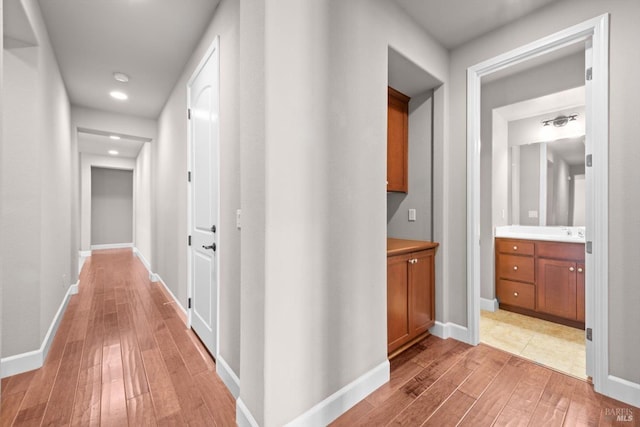 hallway featuring baseboards, light wood finished floors, and recessed lighting