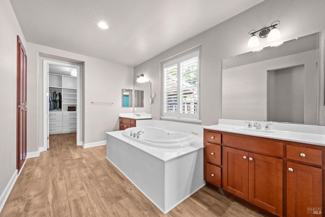 full bathroom with a bath, a sink, two vanities, a walk in closet, and wood finished floors
