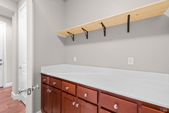 clothes washing area with light wood finished floors and baseboards